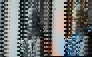 a young woman sitting in a cafe with a coffee in hand, looking outside the window. 